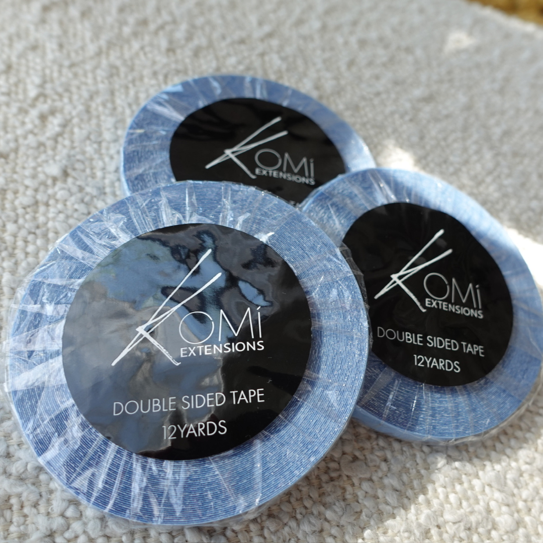 Three rolls of Komi Extensions double-sided tape on a textured surface