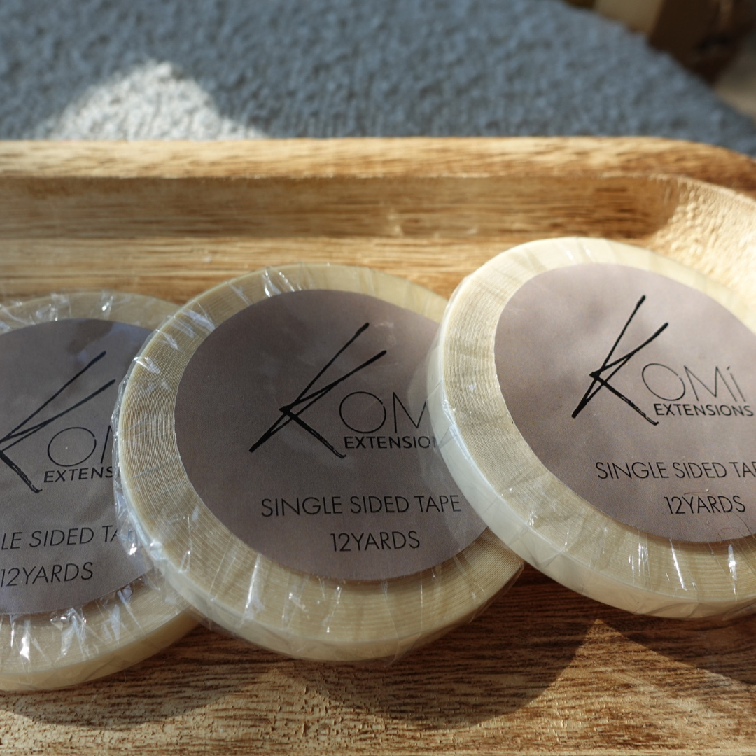 Komi Extensions Single-Sided Replacement Tape rolls displayed on a wooden tray in natural lighting.