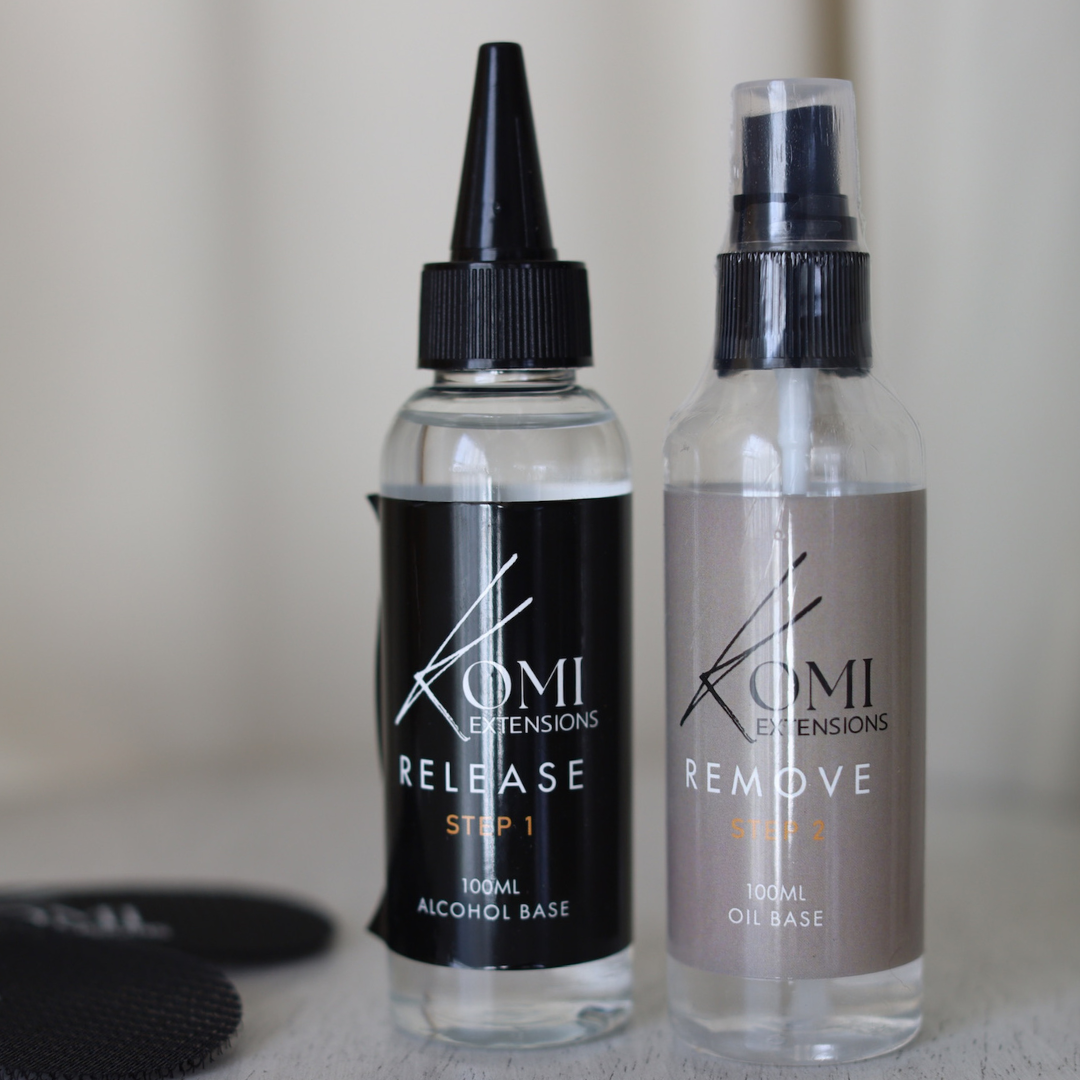Two bottles of Komi Extensions hair care products on a neutral background