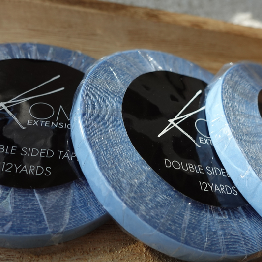 Two rolls of Komi Extensions double-sided tape on a wooden surface