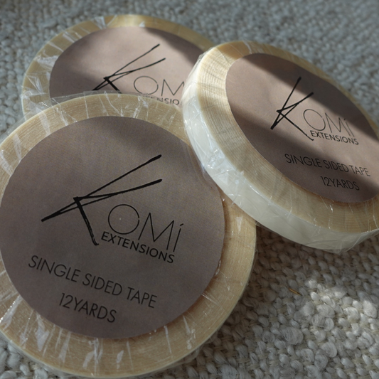 Flat lay of Komi Extensions Single-Sided Replacement Tape rolls with branded labels for hair extensions.