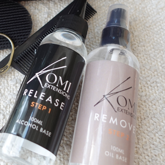 Two bottles of Komi Extensions hair product on a textured surface