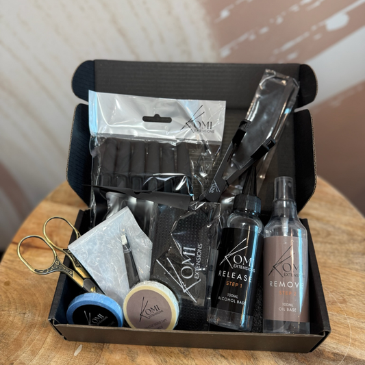 Open Komi Extensions Tape Weft Tool Kit box including remover sprays, scissors, tapes, clips, and professional tools.